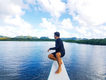 Man sitting on lake against sky
