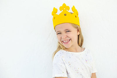 Portrait of smiling girl wearing crown against white wall