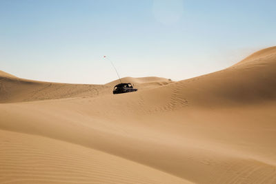 Car on sand in desert against clear sky