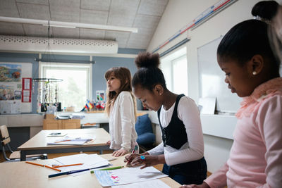 Female students studying while standing at desk in classroom