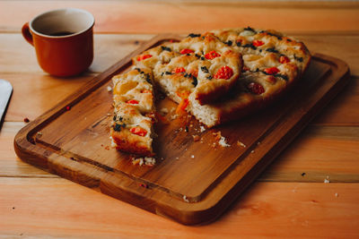 Homemade italian focaccia, with tomato and olive oil and coffee on a rustic wooden background.