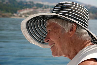 Smiling aged woman wearing hat against lake