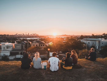 People sitting by buildings against sky during sunset