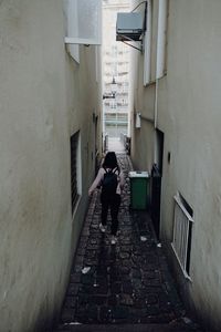 Rear view of woman standing on footpath amidst buildings