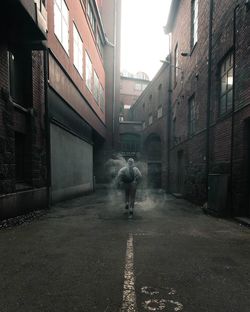 Rear view of man walking through smoke on street amidst buildings