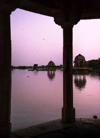 Scenic view of lake by building against sky during sunset