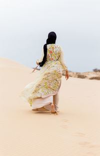 Woman in traditional clothing walking on sand at beach