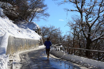 Rear view of person jogging on wet road during winter