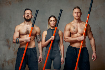 Portrait of fighters holding stick against wall