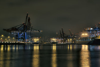 Illuminated cranes over sea against sky at night