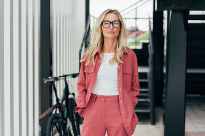 Portrait of an elegant blonde confident woman in glasses standing and looking at the camera person