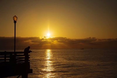 Silhouette man fishing on pier by sea against sky during sunset