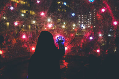 Rear view of silhouette woman touching orb illuminated at night