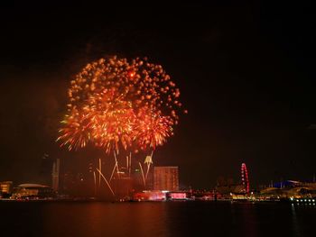 Firework display over illuminated city against sky at night
