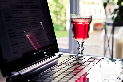 Close-up of red drink in glass by laptop on table 