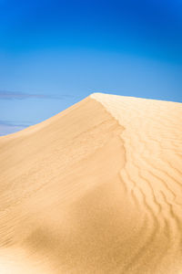 Sand dunes in desert against clear blue sky