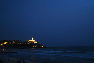 Illuminated building by sea against clear sky at night