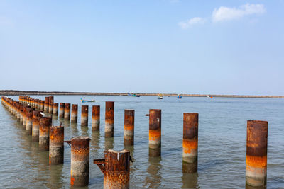 Wooden posts in sea against sky