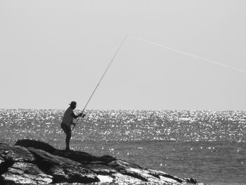 Side view of fisherman fishing at sea shore against clear sky