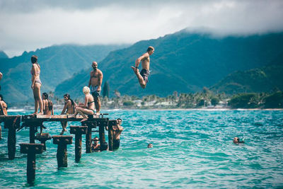 People swimming in sea against mountains