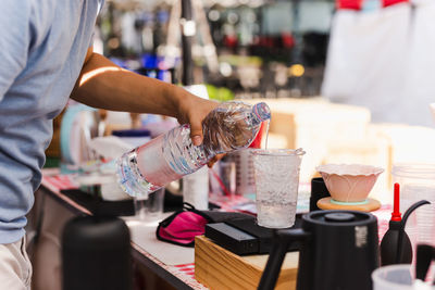 Barista hand pouring water into plastic glass with iced.