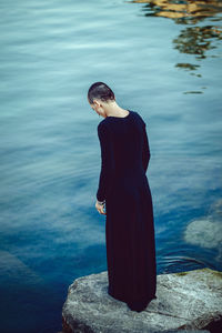 Rear view of woman standing on rock by sea