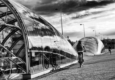 Man cycling in city against sky