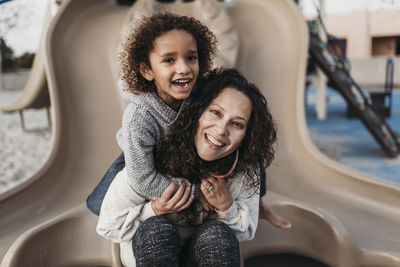 Son embracing mother on slide outside at park playground at dusk