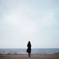 Full length of woman standing on shore at beach against sky