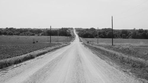 Dirt road amidst agricultural field against clear sky