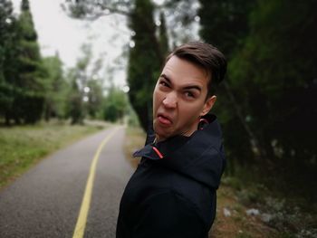 Portrait of young man making face on road against trees