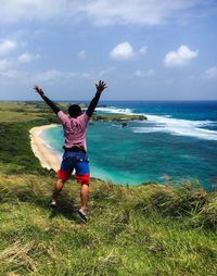 Rear view of man jumping on cliff against sea