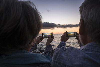 Rear view of couple photographing from mobile phones at beach