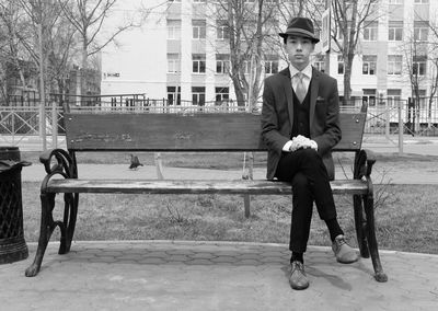 Full length portrait of young man sitting in city