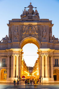 People walking in front of historical building against clear sky during sunset