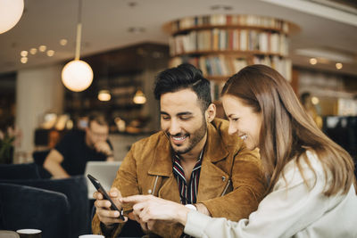 Smiling couple using smart phone while sitting in restaurant