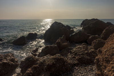 Rocks on beach against sky during sunset