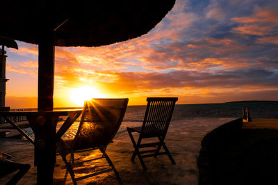 Chairs on beach against sky during sunset