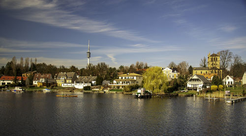 View of buildings by river against cloudy sky