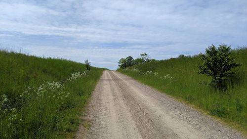 Empty road amidst field against sky
