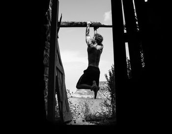 Rear view of woman with arms raised hanging against sky