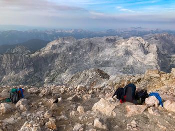 People on rocks by mountains against sky