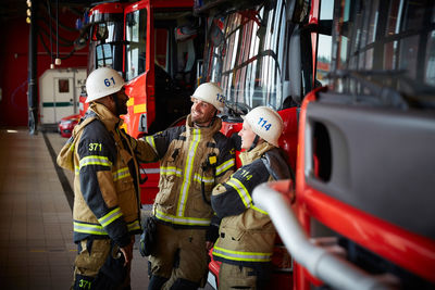 Group of firefighters talking while standing against fire engine at fire station