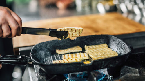 Chef's hand frying sliced tofu cheese in vegan restaurant
