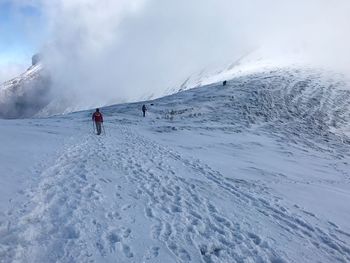 People on snow covered mountain against cloudy sky