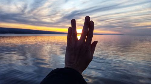 Cropped hand of woman gesturing against sea during sunset