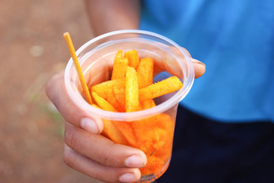 Midsection of person holding french fries in plastic glass