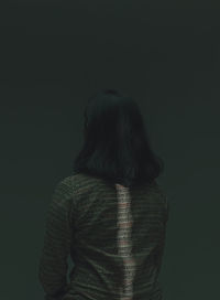 Rear view of woman standing against black background