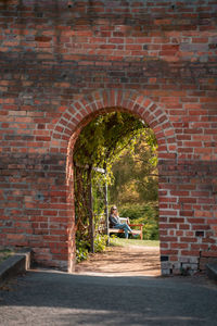 Man sitting on bench against brick wall