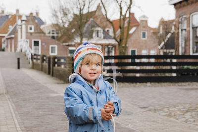 Portrait of boy standing in snow against buildings in city